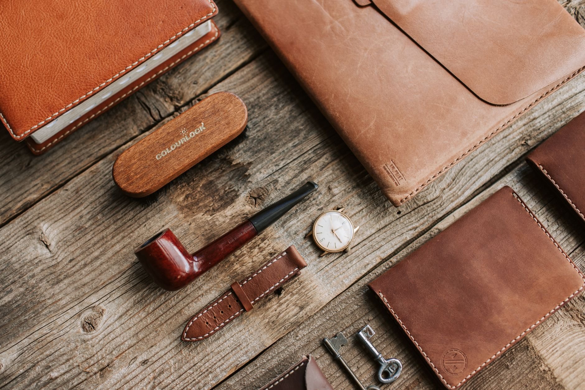 High-quality leather goods arranged on rustic wooden surface with a classic watch